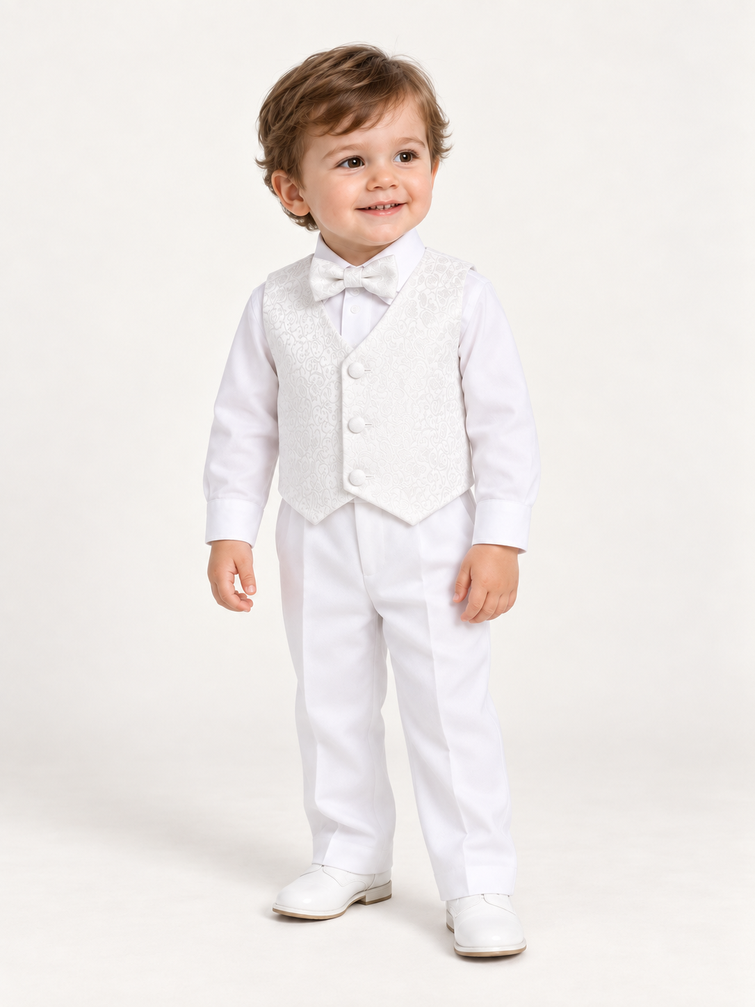 Toddler boy wearing the white 8590 baptism outfit with jacquard vest, bow tie, long-sleeve shirt and trousers.