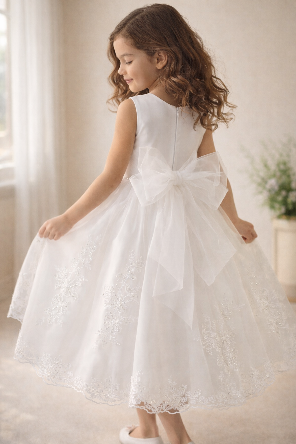 Young girl in a white communion dress standing indoors with a neutral background