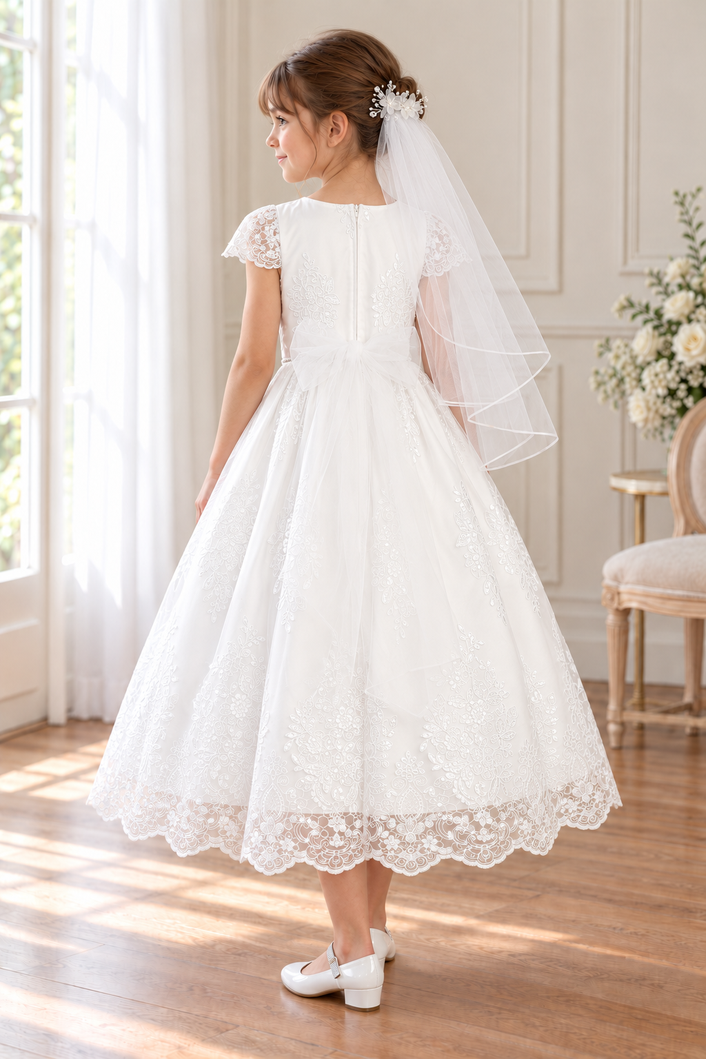 Style 207 white Communion dress rear on a child model, showing lace cap sleeves, floral embroidery and a sheer tulle waist bow; Mia shoes and T-302 organza-flower comb veil sold separately.