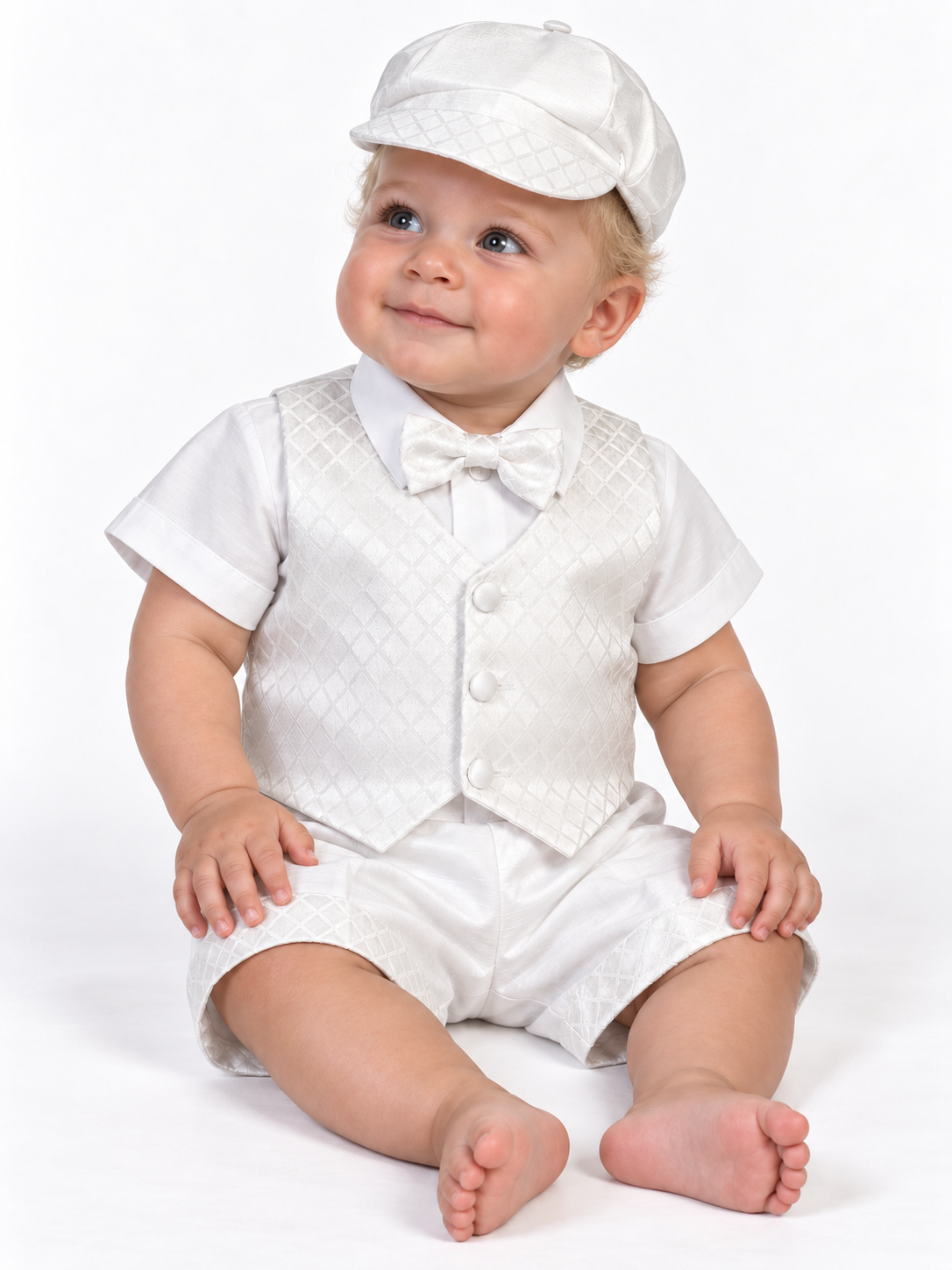 Baby model wearing the Jasper white baptism outfit with diamond jacquard vest, bow tie, matching cap and cuffed shorts.