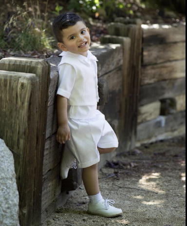 Charming Baby Boys Baptism Outfit with vest, bow tie, and shorts in white, worn by toddler outdoors. Ideal for special ceremonial occasions.