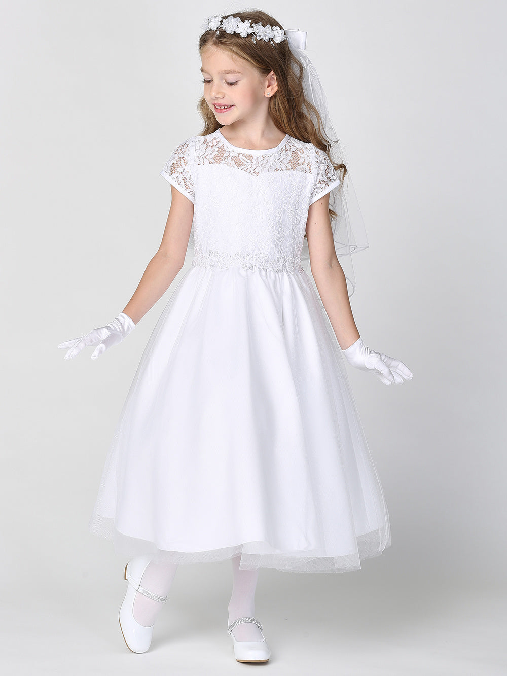 A girl wearing an elegant white First Communion Dress with a lace bodice and tulle skirt.