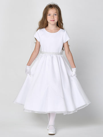 A girl wearing an elegant white First Communion Dress with a satin bodice and crystal organza skirt, adorned with diamonds and pearls on the waistline.