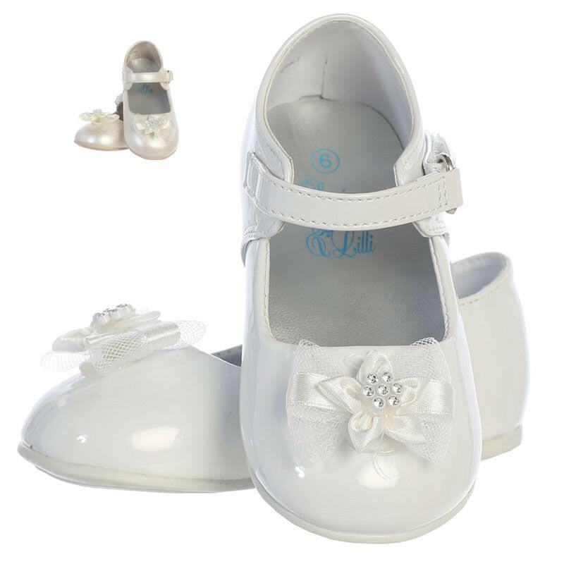 Communion shoes for girls in white with bow and rhinestone detail, ideal for flower girl or baptism outfits. Features glossy finish and ankle strap.
