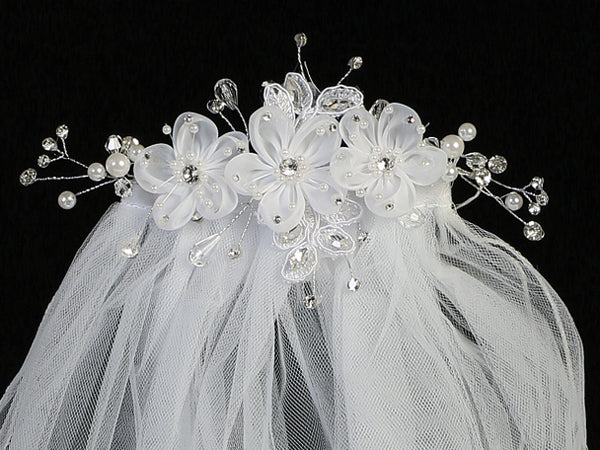 Close-up of 24" Communion veil with organza flowers, rhinestones, pearls, and crystals on a white headpiece. Elegant floral detailing adds charm.