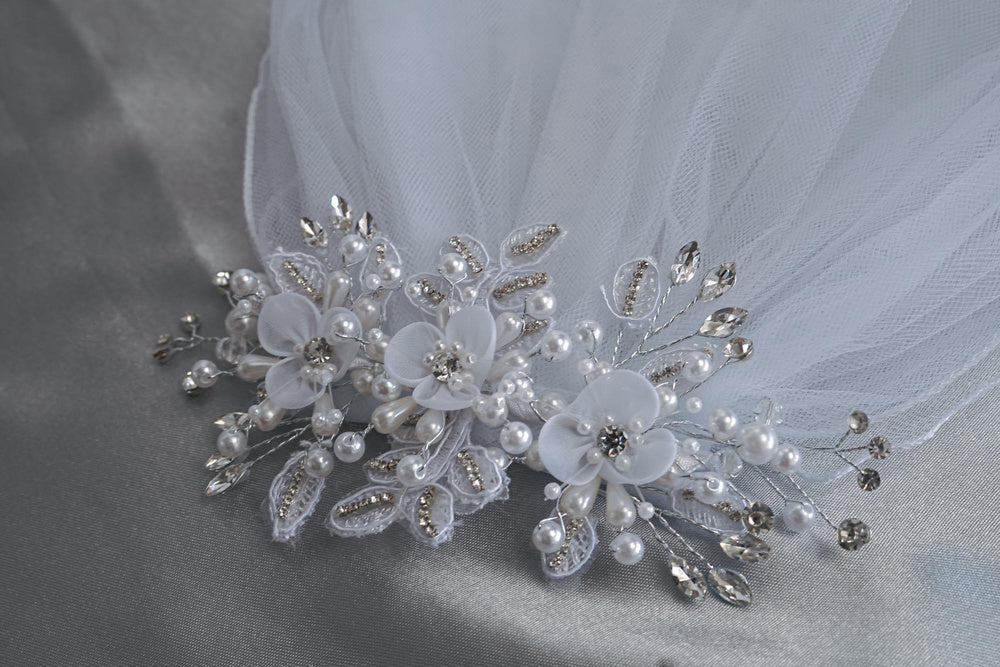 Close-up of 24" Communion veil featuring intricate organza flowers, pearls, and rhinestones on satin background. Elegant religious accessory.