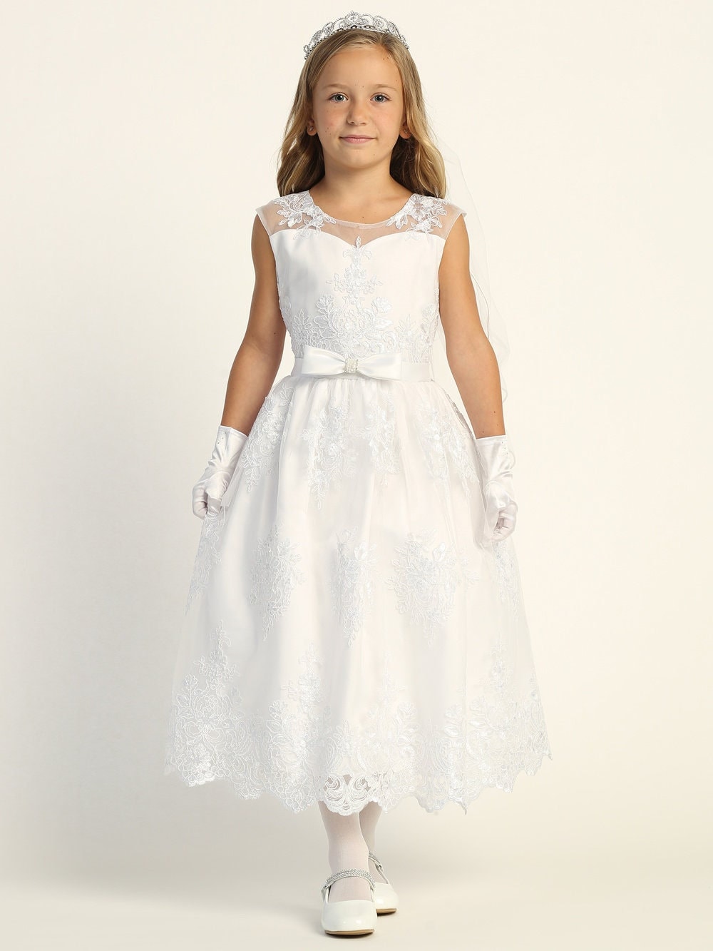 A girl wearing an exquisite white First Communion Dress with corded embroidered tulle and sequins, featuring a bow accent on the waist. (This is the actual image from the listing)