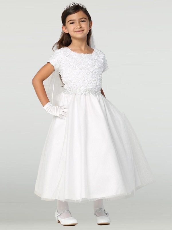A girl wearing a dazzling white First Communion Dress with a sequined bodice and glitter tulle skirt.