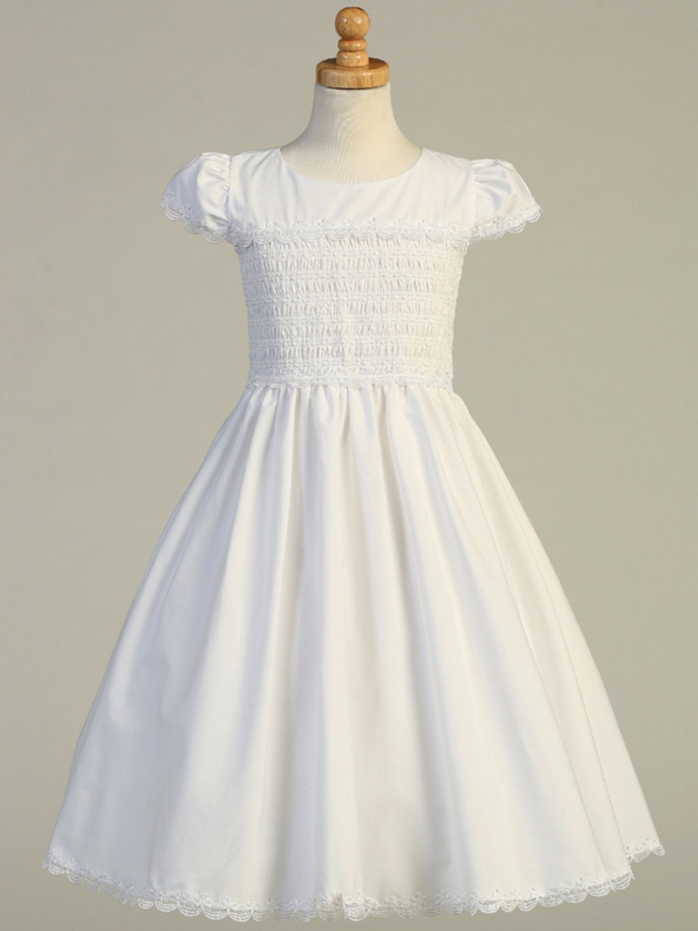 Girls White First Communion Dress on mannequin with smocked cotton bodice, lace-trimmed hem, and puff sleeves for traditional elegance.