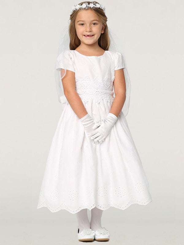 A girl wearing a charming white First Communion Dress made of cotton eyelet fabric.