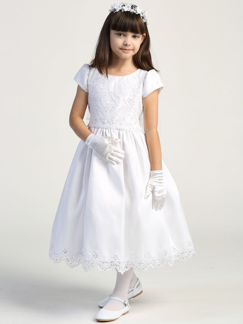 A girl wearing a stunning white First Communion Dress with embroidered lace and sequins on the tulle bodice. 
